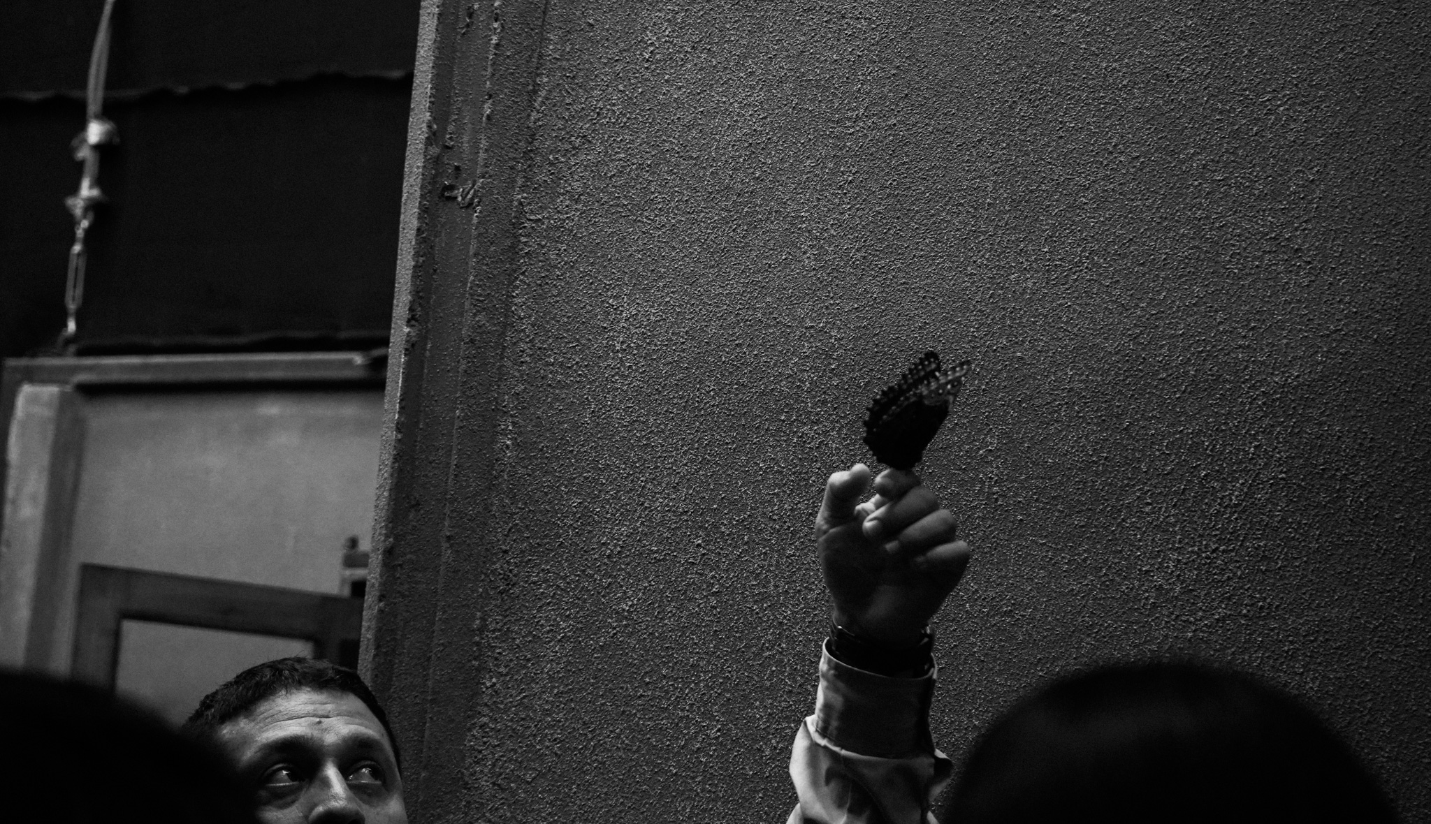 Man's fist raised holding prayer beads against a dark wall