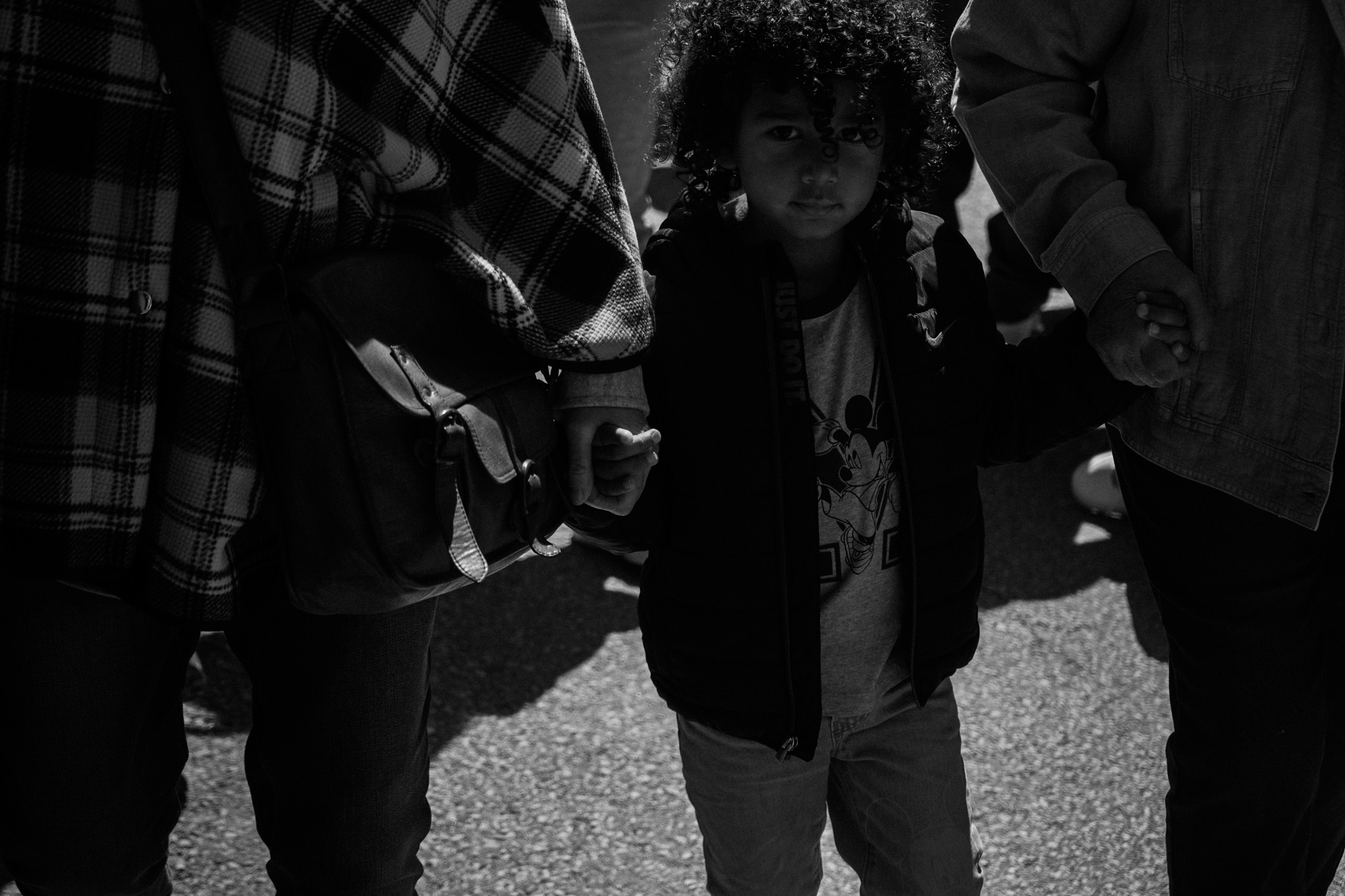 Child walking between two adults, looking directly at the camera