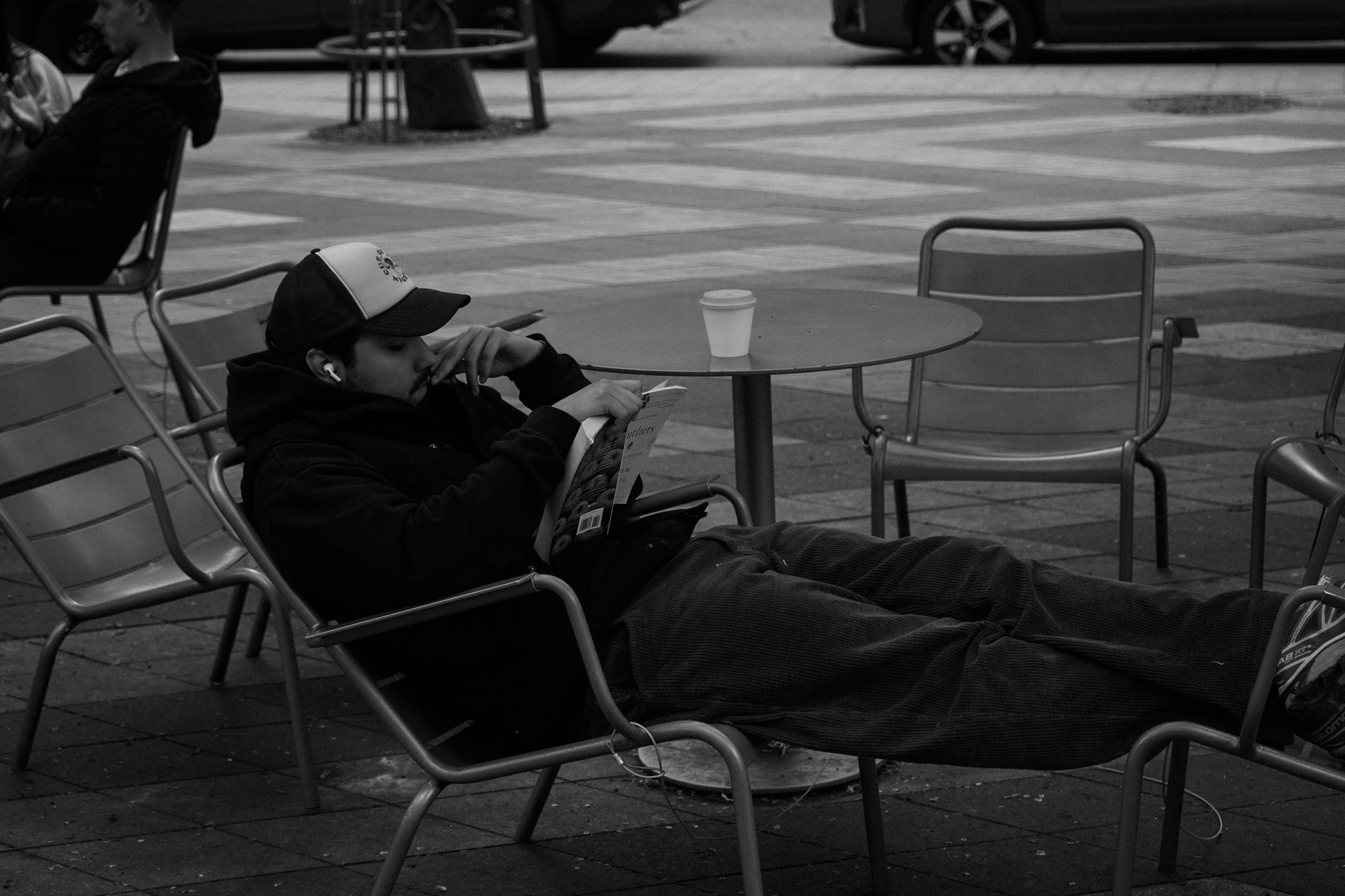 Person sprawled across two cafe chairs, reading