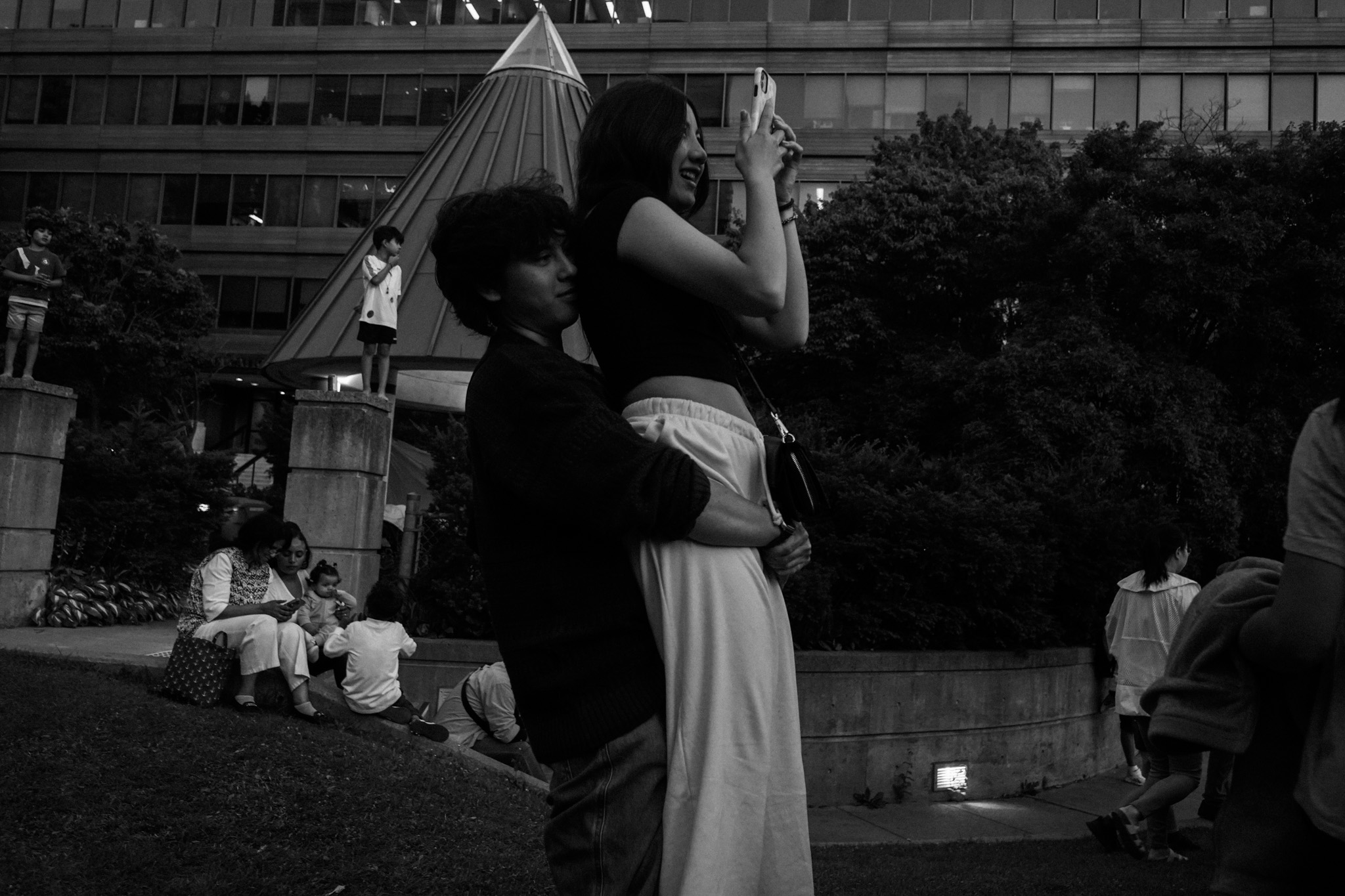 Young couple embracing at night, city buildings and a family in the background