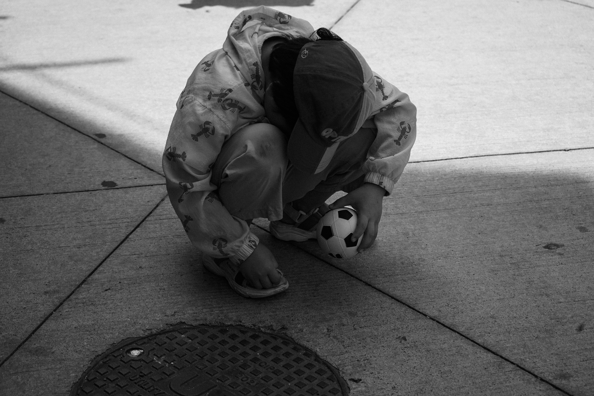 Child crouching alone on the sidewalk, clutching a small ball