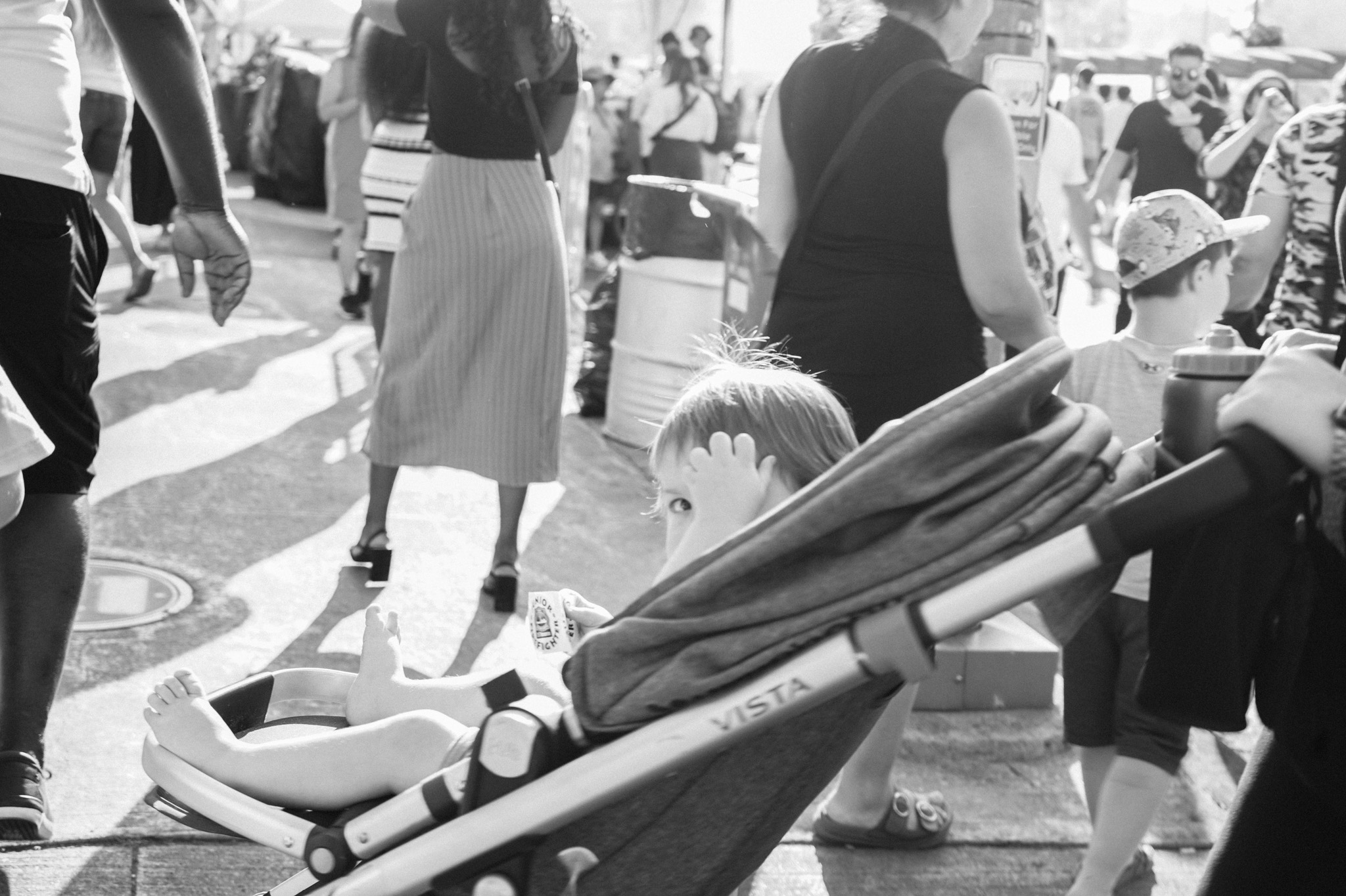 Child in a stroller peeking out at a crowded market, hand raised