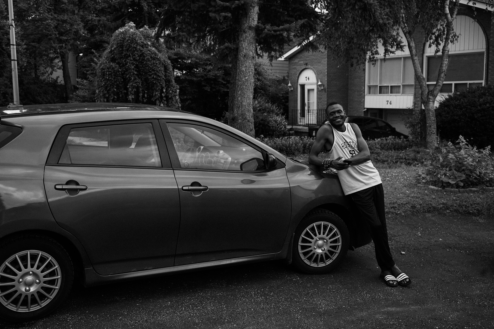 Man leaning on a car in a residential street, smiling