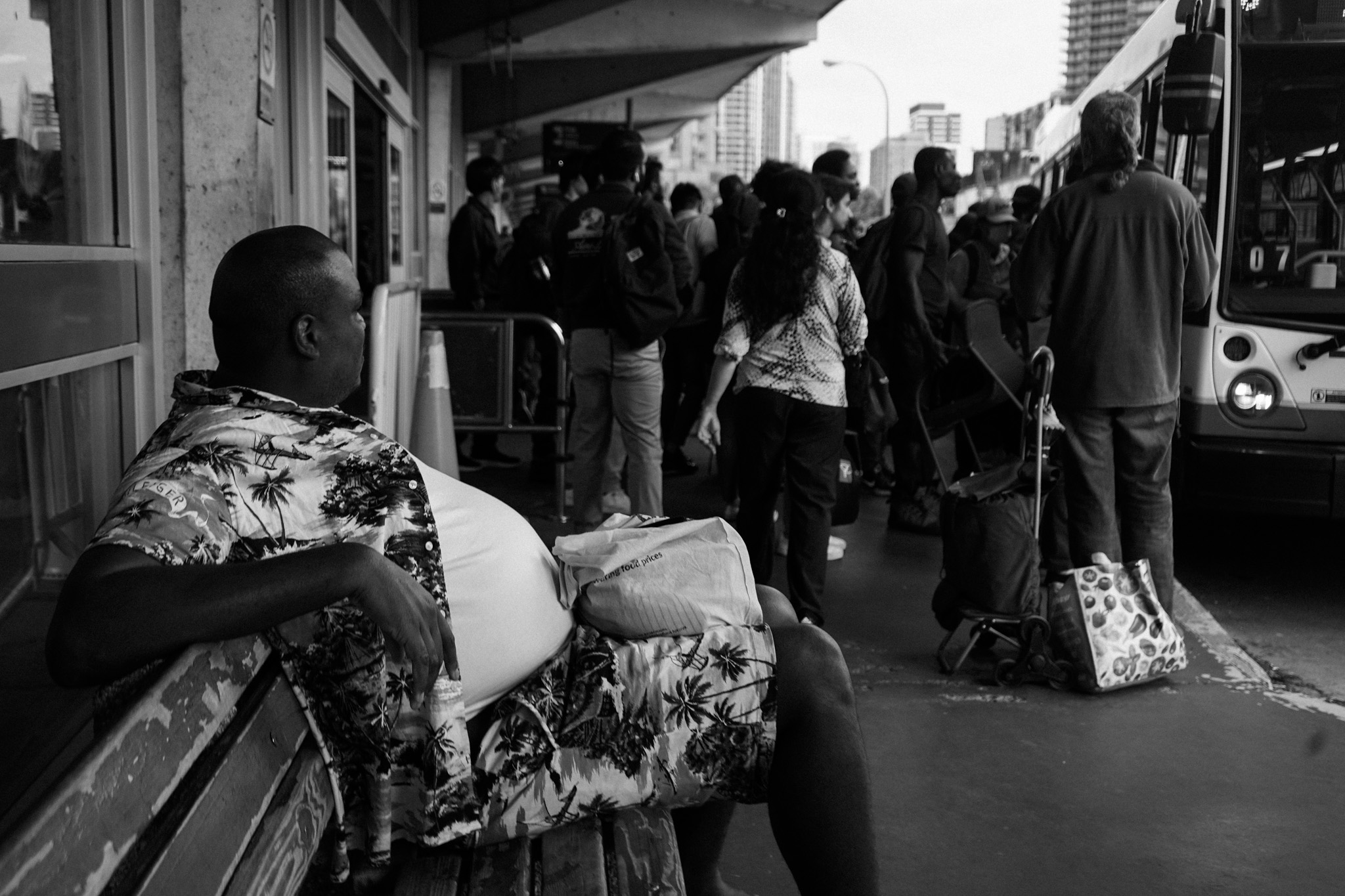 Man sitting at a bus stop watching the crowd board