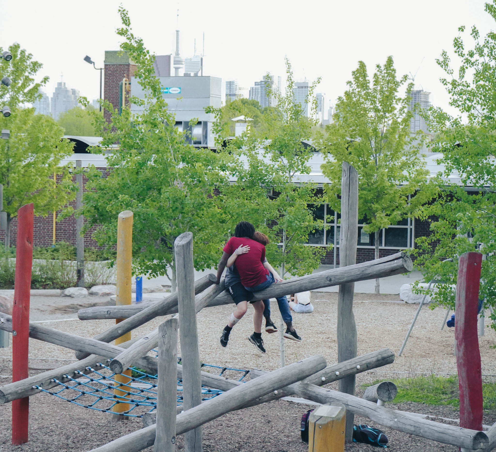Two children climbing on a wooden playground structure, Toronto skyline behind