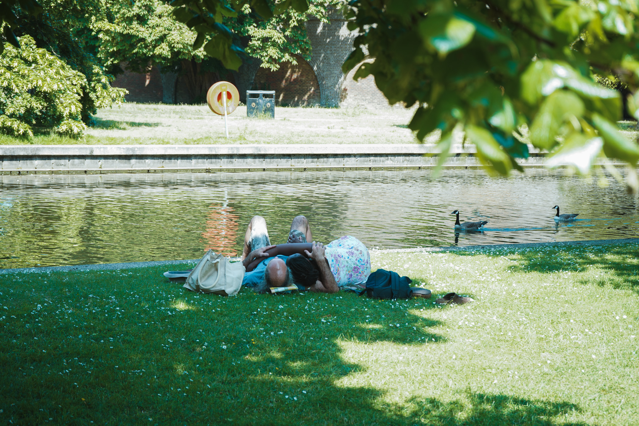 Couple lying on the grass by a pond, watching ducks in summer light