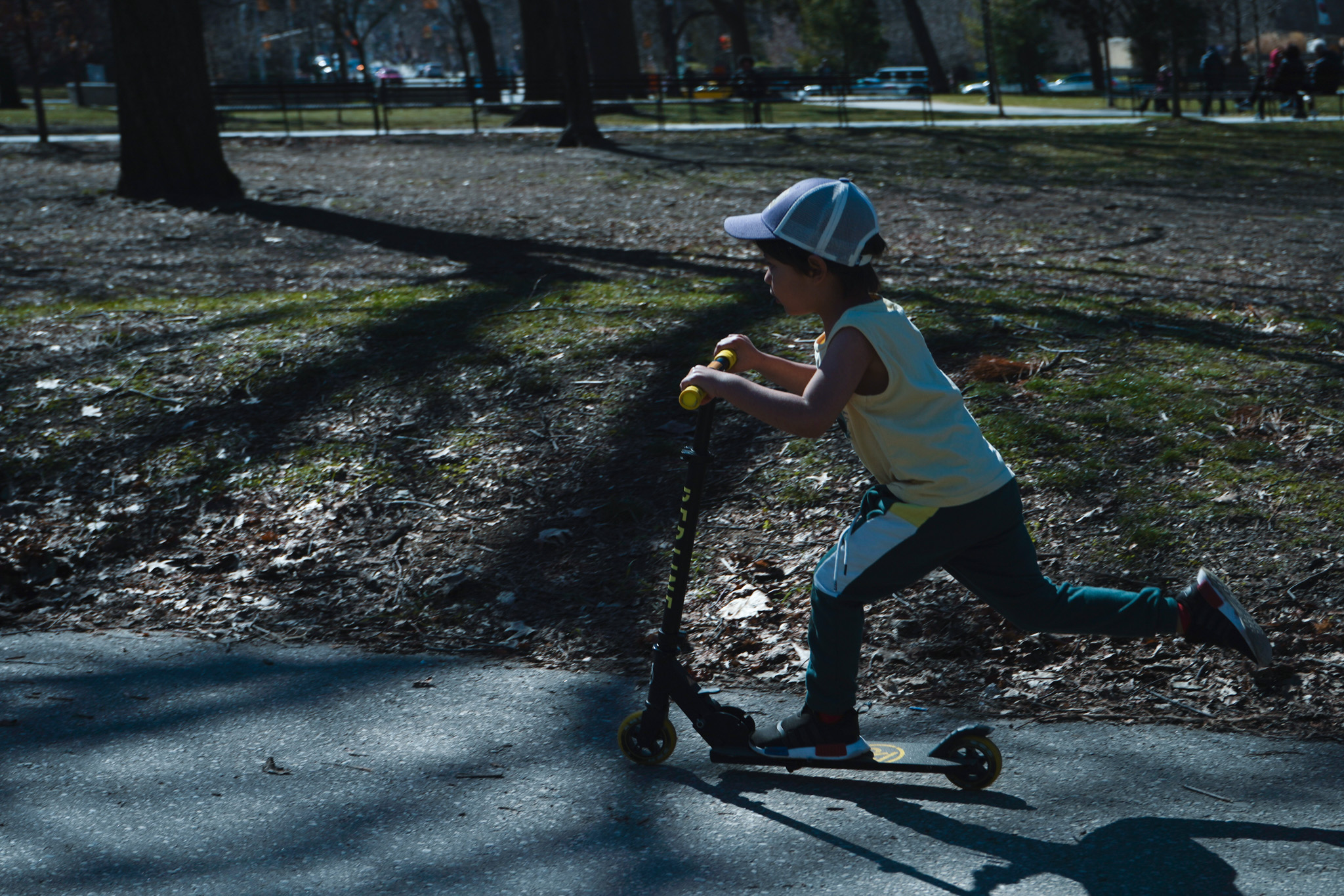 Child on a scooter in a park, pushing forward through tree shadows