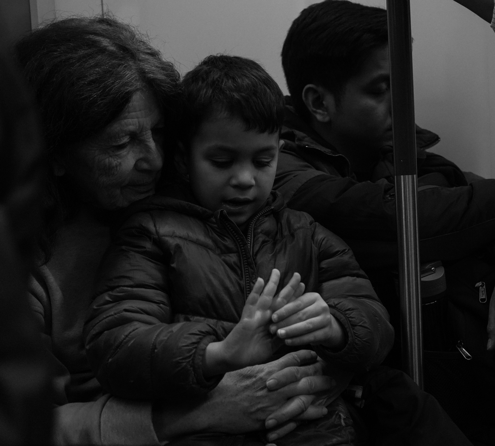 Child held close by grandmother on the metro, both looking down at their intertwined hands