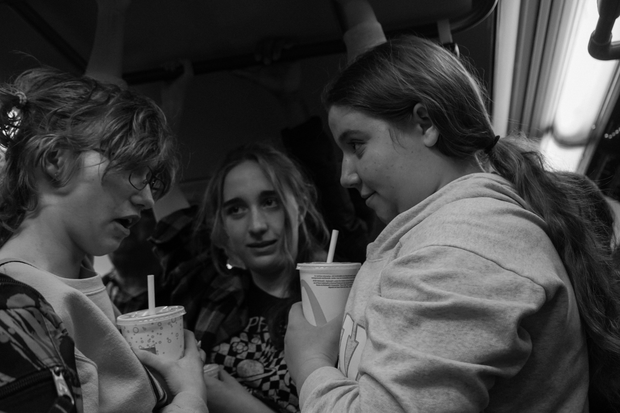 Three teenagers huddled together with drinks on the subway