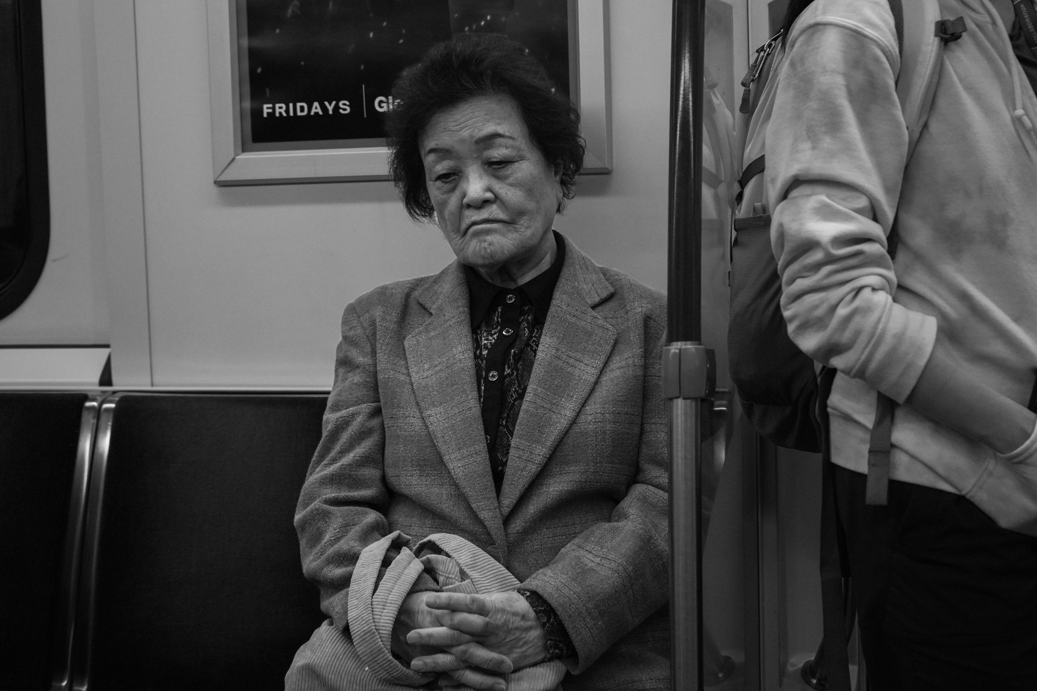 Elderly woman sitting alone, hands clasped, pensive